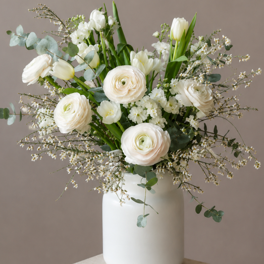 Luxury white ranunculus and tulip flower arrangement in a modern white ceramic vase with eucalyptus by BLÜM Miami